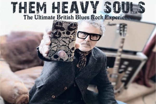 Promotional image for Them Heavy Souls, “The Ultimate British Blues Rock Experience,” featuring a man in sunglasses holding a decorated effects pedal toward the camera, with a guitar blurred in the background.