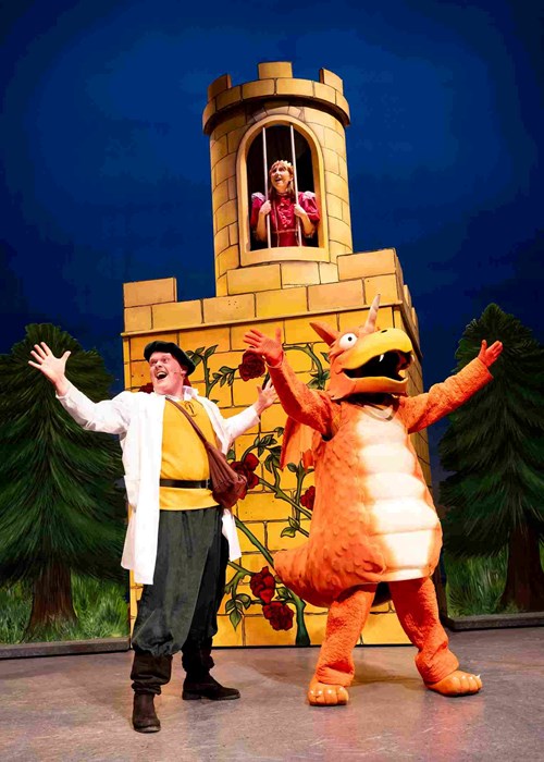 Zog and Sir Gadabout stand at the bottom of a tower with their arms outstretched. Above them, at a window behind bars, is Princess Pearl who looks happy. 
