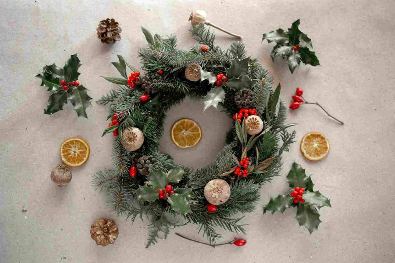 Handmade evergreen Christmas wreath decorated with holly, red berries, pine cones, dried orange slices and natural seed pods.