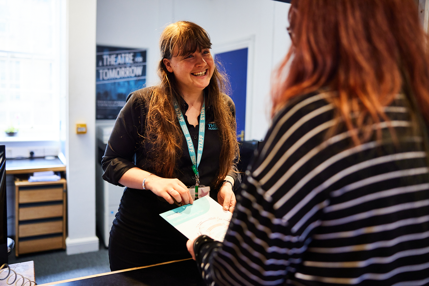 Woman with long brown hair smiling over the counter at a customer