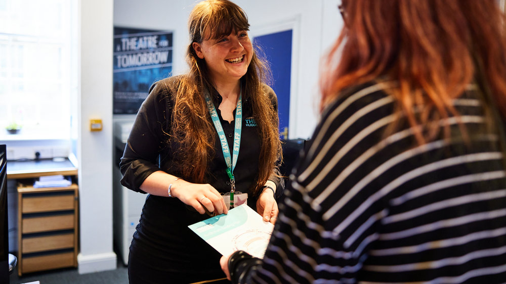 Woman with long brown hair smiling over the counter at a customer