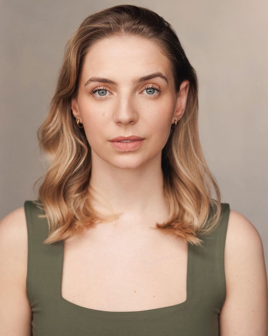 Lauren Bickerdike: Woman with shoulder-length blonde hair and blue eyes, wearing a sleeveless olive green top, looking calmly at the camera against a neutral background.