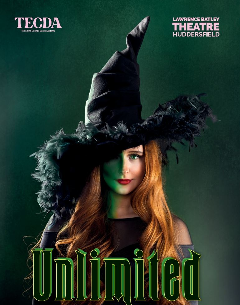 A young woman with long red hair wears a dramatic black witch hat trimmed with feathers, partially shadowing her face against a dark green background.