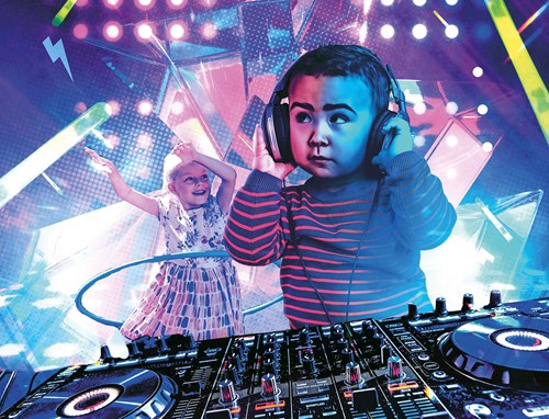 A child wearing headphones stands behind a DJ mixing desk. There is another young person in the background dancing using a hula-hoop